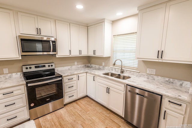 kitchen with sink, light stone counters, light hardwood / wood-style flooring, stainless steel appliances, and white cabinets