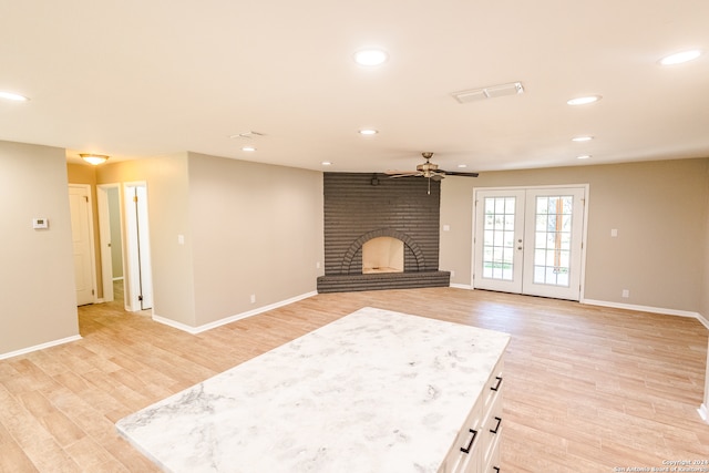 unfurnished living room featuring french doors, ceiling fan, a fireplace, and light wood-type flooring