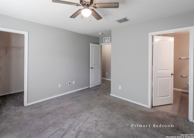 unfurnished bedroom featuring ceiling fan, dark colored carpet, a closet, and a spacious closet