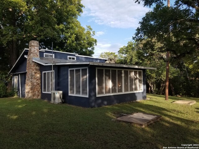 rear view of property with central air condition unit, a sunroom, and a lawn