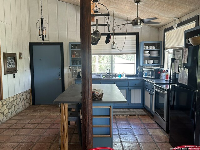 kitchen with wood walls, ceiling fan, stainless steel appliances, dark tile flooring, and sink