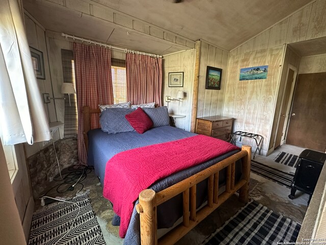 bedroom featuring vaulted ceiling and wooden walls