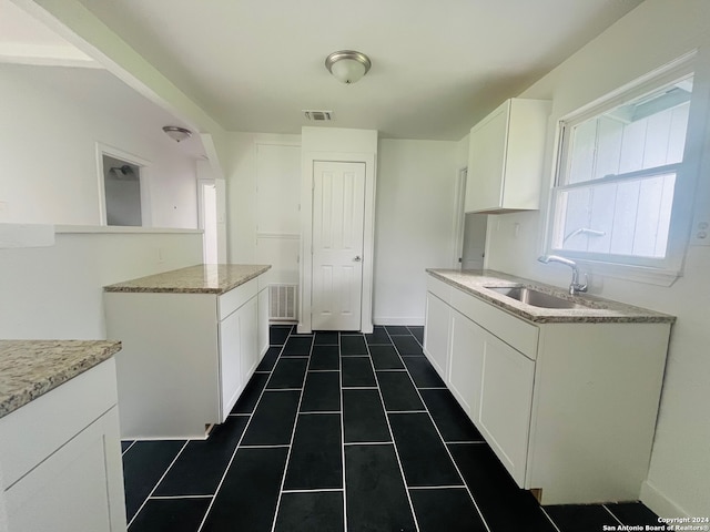 kitchen featuring a center island, dark tile floors, white cabinets, light stone countertops, and sink