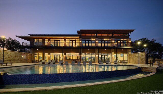 back house at dusk featuring a patio and a balcony