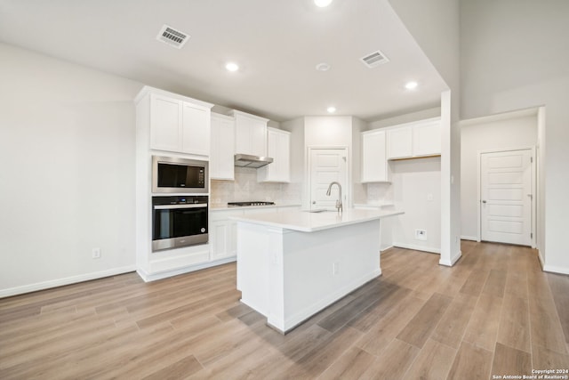 kitchen featuring a center island with sink, white cabinetry, built in microwave, and stainless steel oven