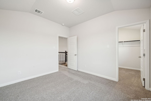 unfurnished bedroom featuring a closet, a walk in closet, light carpet, and vaulted ceiling