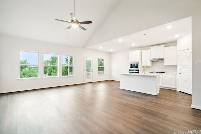 kitchen featuring a kitchen island with sink, high vaulted ceiling, decorative backsplash, white cabinets, and black appliances