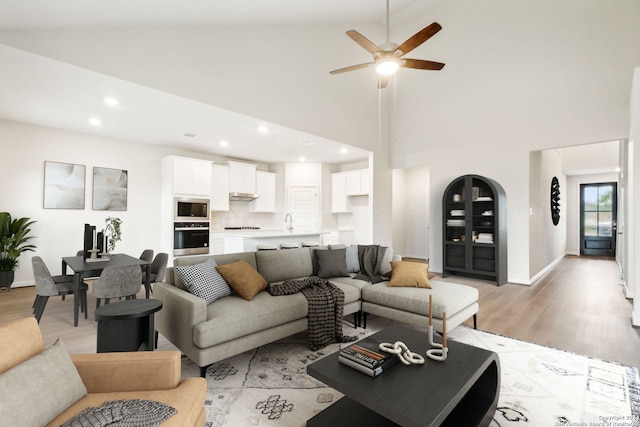 living room featuring ceiling fan, a high ceiling, and light hardwood / wood-style flooring