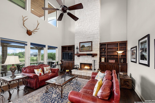 living room with dark hardwood / wood-style flooring, ceiling fan, a stone fireplace, and a towering ceiling