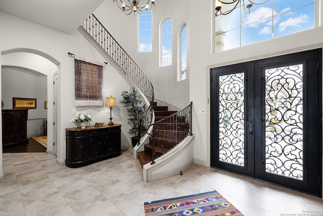 foyer entrance featuring french doors, light tile floors, a high ceiling, and an inviting chandelier