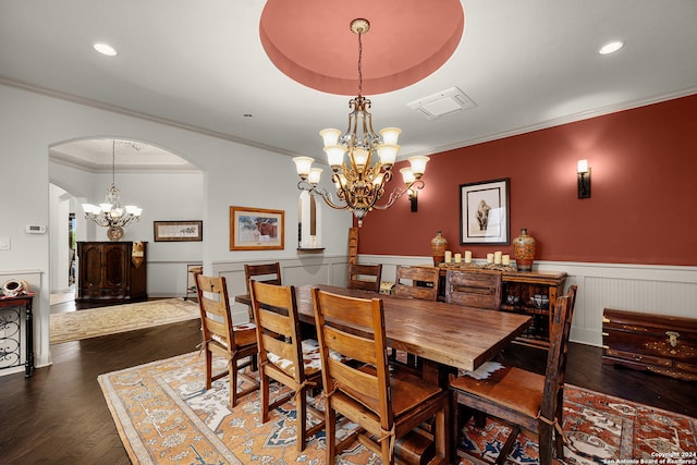 dining area with dark wood-type flooring, a tray ceiling, an inviting chandelier, and crown molding