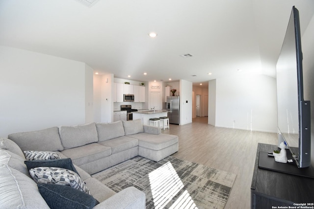 living room featuring lofted ceiling, light wood finished floors, visible vents, and recessed lighting