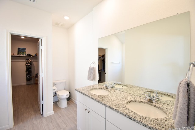 bathroom with toilet, wood finished floors, a sink, a spacious closet, and double vanity