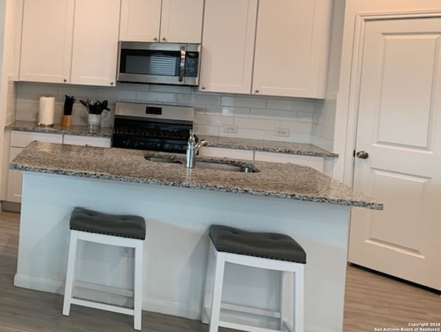 kitchen with light hardwood / wood-style floors, stove, tasteful backsplash, light stone counters, and white cabinets