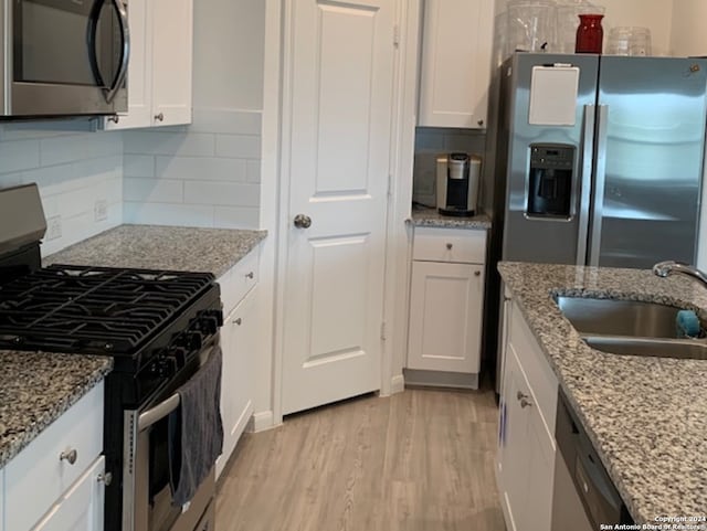 kitchen featuring light wood-type flooring, appliances with stainless steel finishes, tasteful backsplash, and white cabinetry