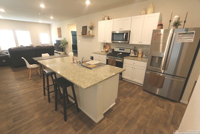 kitchen featuring a kitchen breakfast bar, dark hardwood / wood-style flooring, white cabinetry, appliances with stainless steel finishes, and a center island with sink