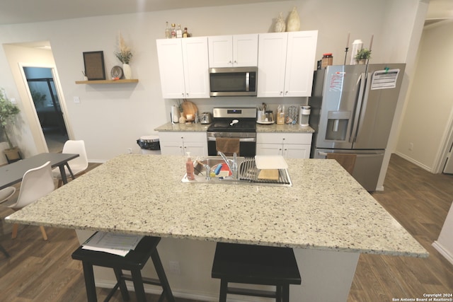 kitchen with white cabinets, a kitchen bar, dark wood-type flooring, stainless steel appliances, and an island with sink