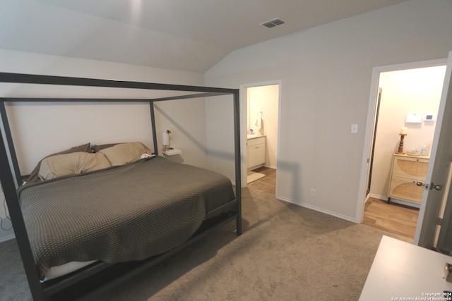 bedroom with light colored carpet, vaulted ceiling, and ensuite bathroom