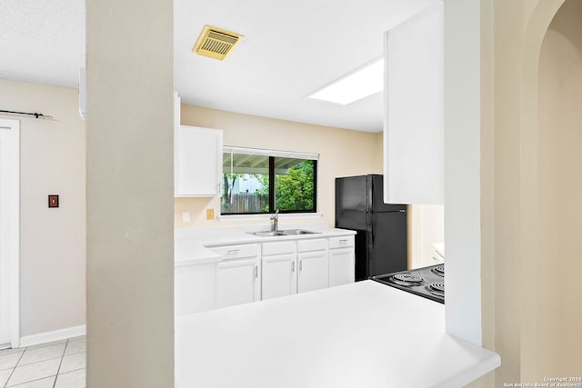 kitchen with white cabinets, sink, black refrigerator, and light tile flooring