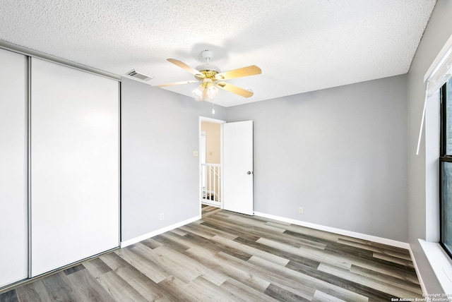 empty room with ceiling fan, light wood-type flooring, and a textured ceiling