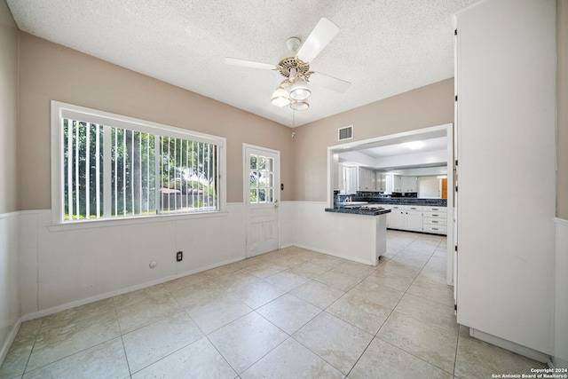 tiled empty room featuring ceiling fan, a textured ceiling, and plenty of natural light