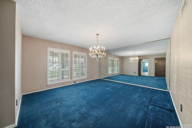 carpeted empty room featuring a textured ceiling and a chandelier