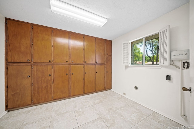 interior space featuring electric dryer hookup, a textured ceiling, light tile patterned floors, and cabinets