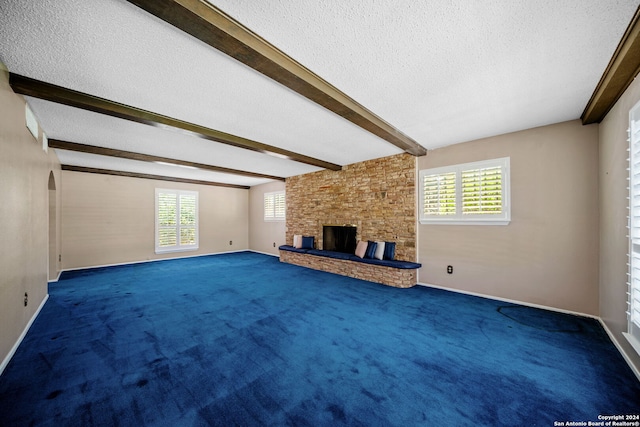 unfurnished living room with beamed ceiling, a fireplace, a wealth of natural light, and carpet floors