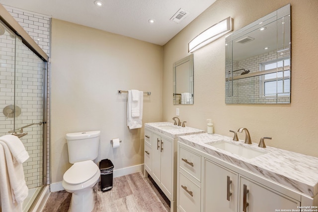 bathroom with dual vanity, a shower with shower door, hardwood / wood-style flooring, toilet, and a textured ceiling