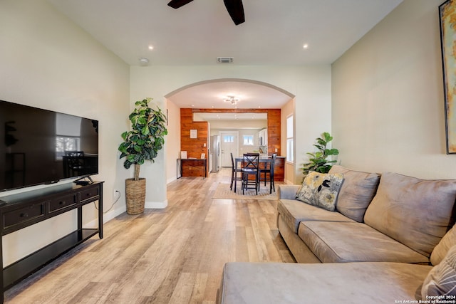 living room featuring ceiling fan, light wood-type flooring, and wooden walls