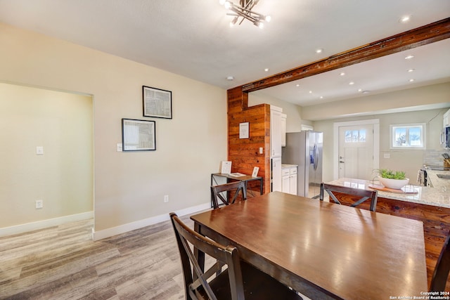 dining room with wooden walls, beam ceiling, and light wood-type flooring