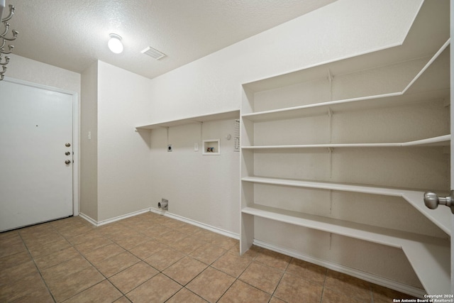 laundry room featuring hookup for an electric dryer, light tile floors, hookup for a washing machine, and a textured ceiling