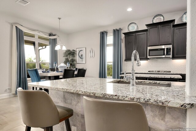 kitchen featuring light stone counters, tasteful backsplash, a kitchen bar, and decorative light fixtures