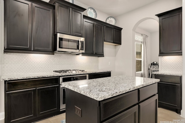 kitchen featuring light stone counters, appliances with stainless steel finishes, a center island, light tile floors, and tasteful backsplash