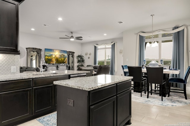 kitchen featuring ceiling fan, backsplash, a kitchen island, and light stone countertops