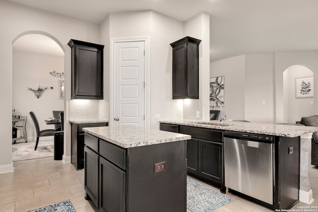 kitchen featuring a kitchen island, tasteful backsplash, light tile flooring, and stainless steel dishwasher