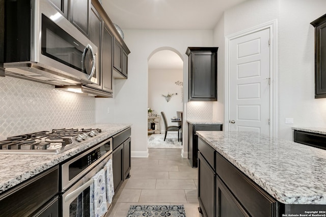 kitchen with light stone countertops, light tile flooring, stainless steel appliances, tasteful backsplash, and dark brown cabinetry