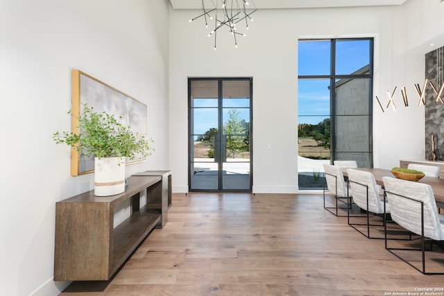 doorway to outside featuring french doors, wood-type flooring, a towering ceiling, and a notable chandelier