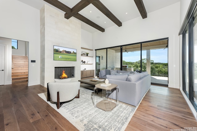 living room featuring a large fireplace, dark hardwood / wood-style flooring, beam ceiling, and a towering ceiling