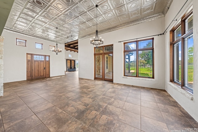 spare room with plenty of natural light, dark tile flooring, an inviting chandelier, and a high ceiling