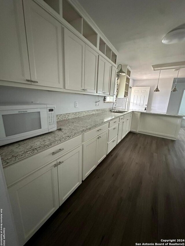 kitchen featuring light stone countertops, sink, dark hardwood / wood-style flooring, white cabinetry, and decorative light fixtures