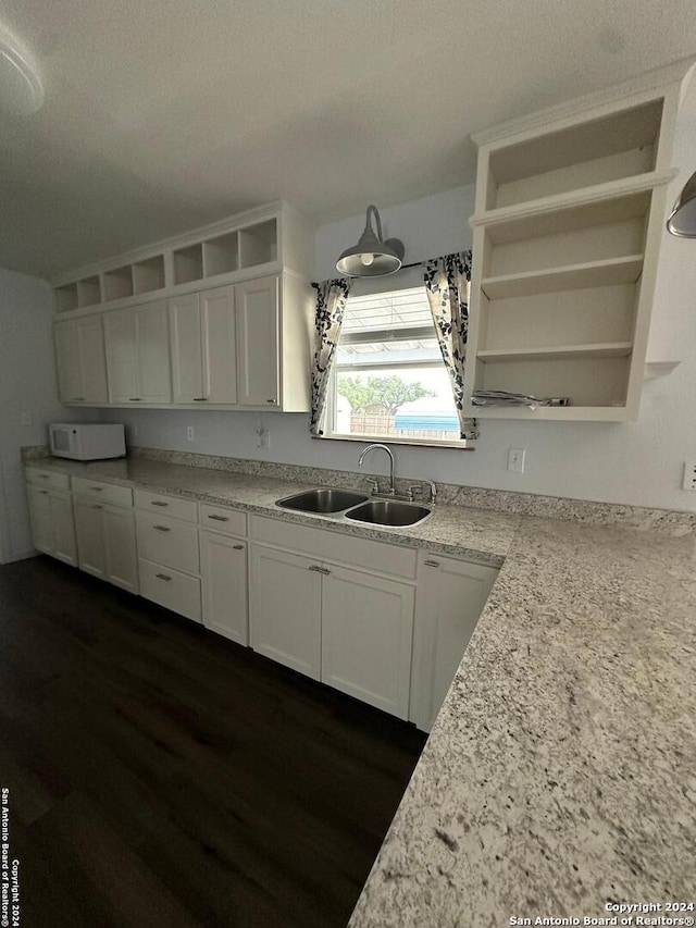 kitchen with white cabinets, a textured ceiling, light stone countertops, dark hardwood / wood-style floors, and sink