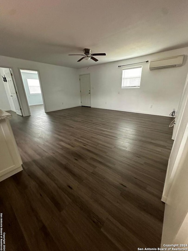 spare room with an AC wall unit, dark wood-type flooring, plenty of natural light, and ceiling fan