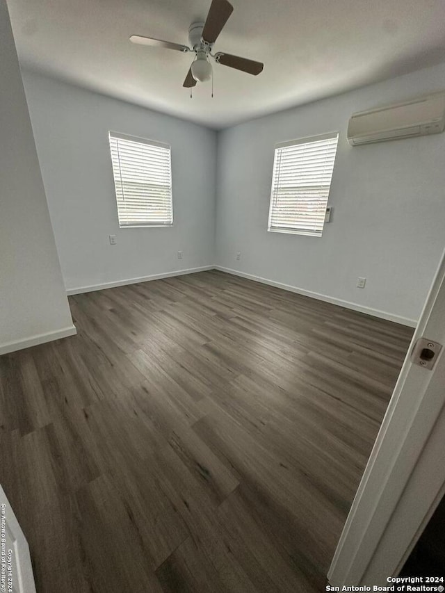 empty room featuring dark wood-type flooring, a wall mounted AC, a healthy amount of sunlight, and ceiling fan