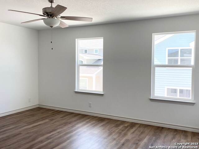 empty room with ceiling fan, dark hardwood / wood-style flooring, and plenty of natural light