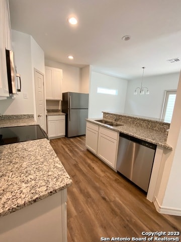 kitchen featuring light stone countertops, stainless steel appliances, white cabinets, pendant lighting, and light wood-type flooring