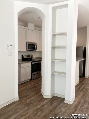 kitchen featuring appliances with stainless steel finishes, white cabinets, dark hardwood / wood-style floors, and light stone counters