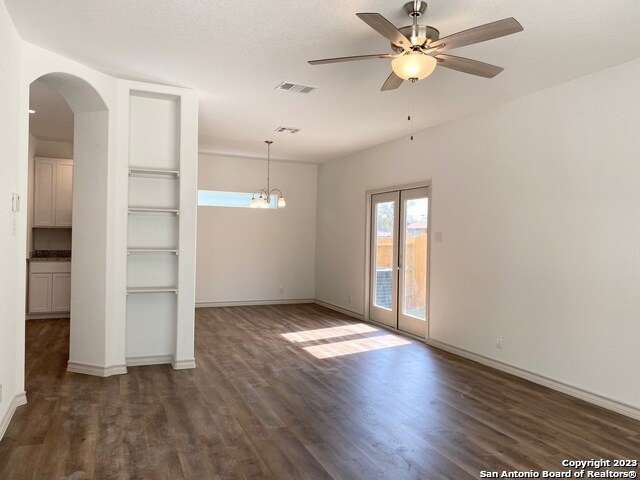 empty room featuring ceiling fan with notable chandelier and dark hardwood / wood-style floors