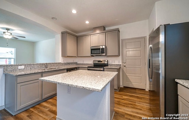 kitchen featuring appliances with stainless steel finishes, gray cabinets, a kitchen island, ceiling fan, and dark hardwood / wood-style flooring