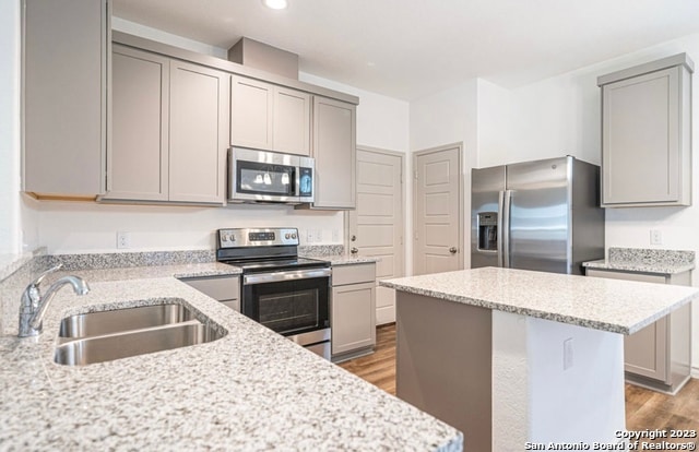 kitchen featuring sink, light wood-type flooring, gray cabinets, stainless steel appliances, and light stone countertops